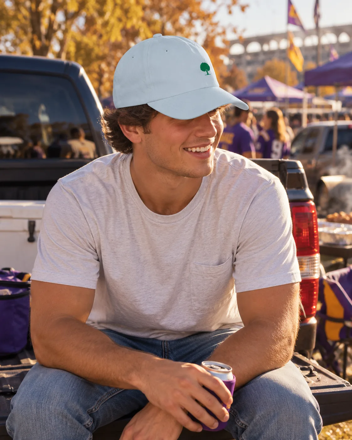 A young man sitting on a truck tailgate at a fall football tailgate, wearing the Oak Dad Hat